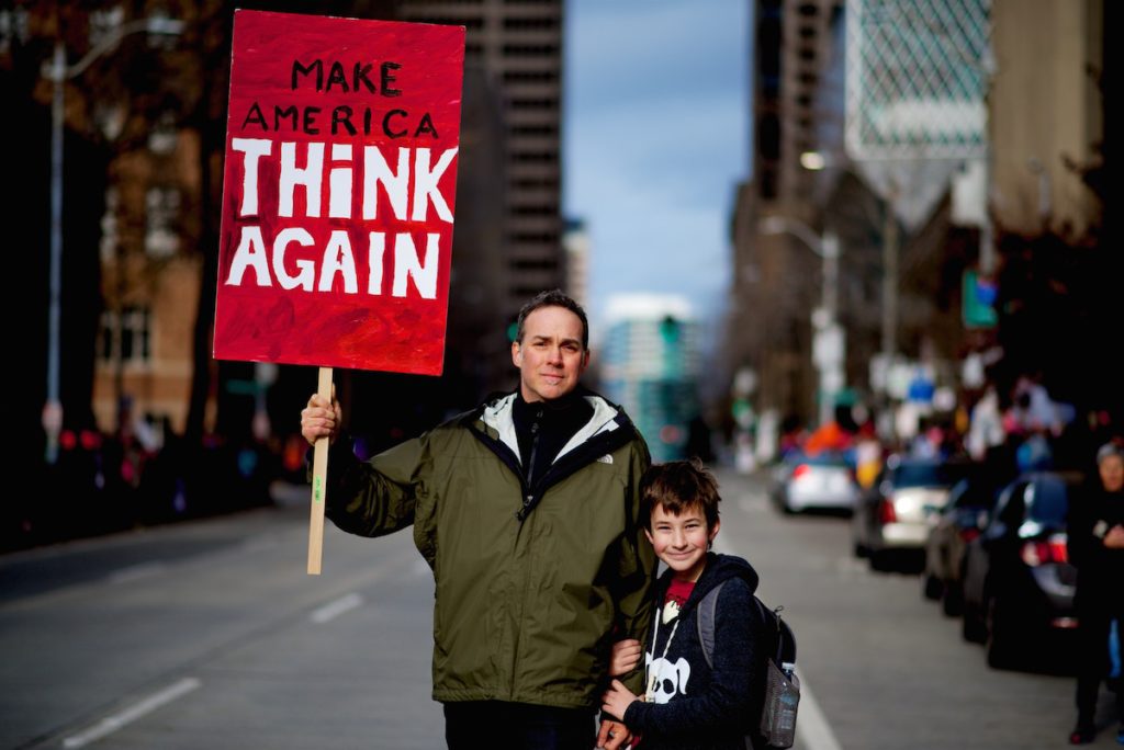 A father and son with sign that says Make America Think Again