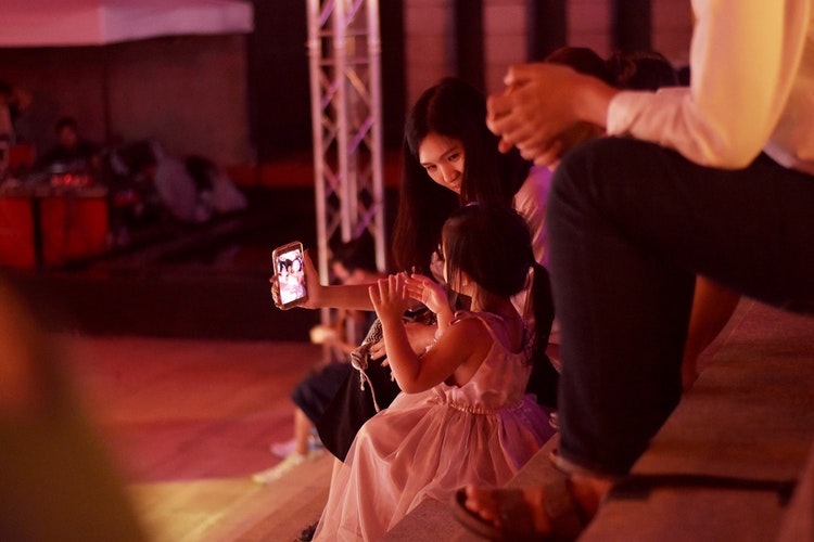 Mother sitting with young girl holding a smart phone taking a photograph