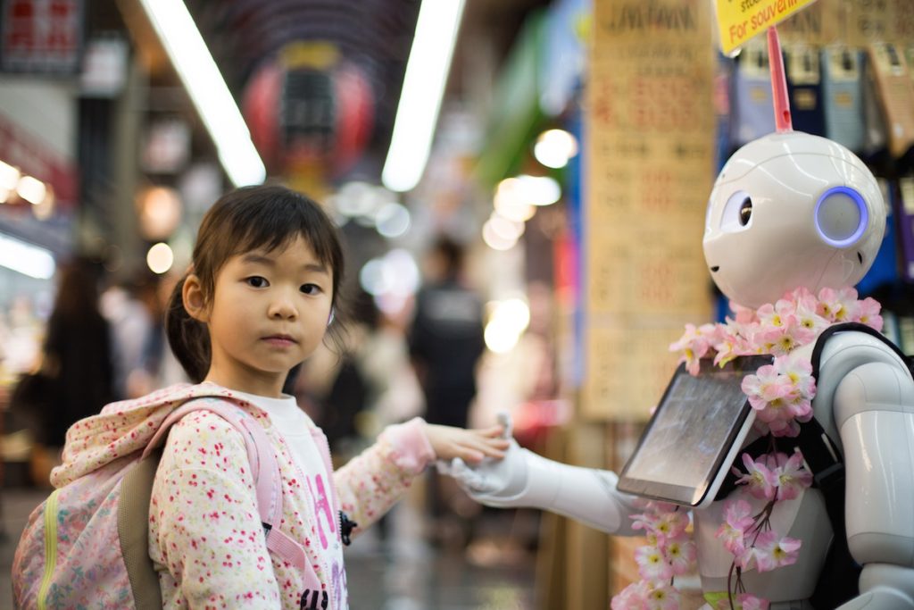 Young child holds hand of small white robot in Japan