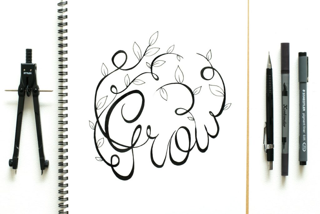 Calligraphy of the word Grow on a sketchpad with pens on the side