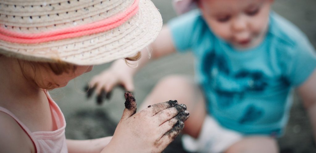 2 young children with sandy hands playing in sand