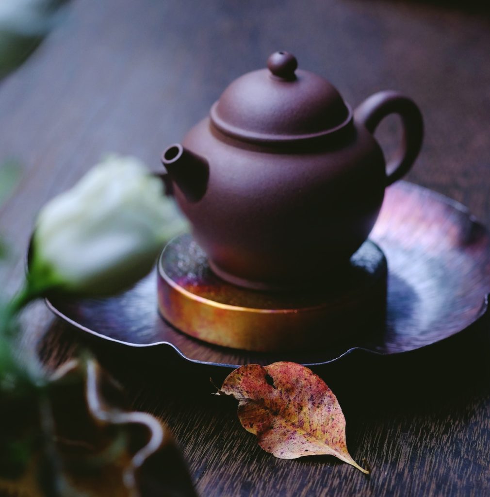 earthware teapot on tray with fall leaf beside it